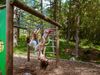 Zwei Kinder spielen und klettern auf einem Naturspielplatz im Wald des Goms an einem sonnigen Tag.